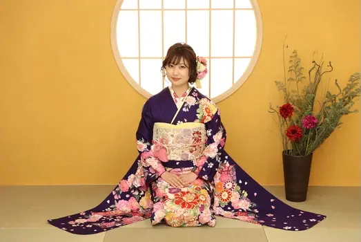 紫色の振袖姿の若い女性が和風窓の前で座る