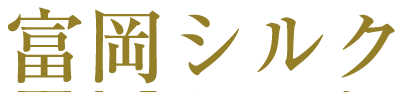 黒い背景に金色で「富岡シルク」と書かれた日本語の漢字と仮名が様式化されています。文字は太字で目立つように表示されており、伝統的でエレガントな書体は古典的な美学を反映しています。