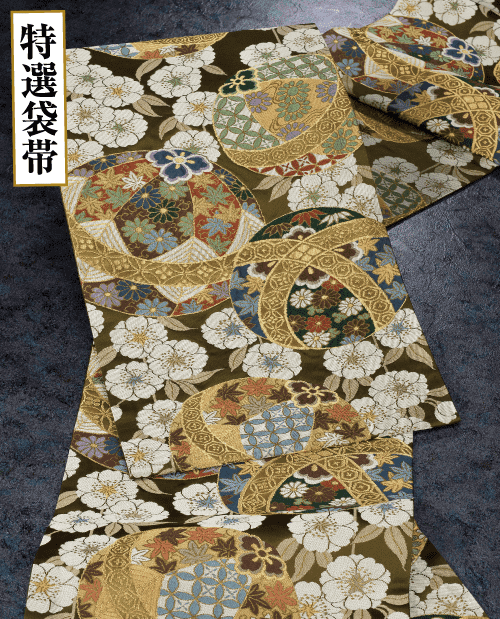 色鮮やかな幾何学模様、花のモチーフ、金色のアクセントが特徴の複雑なデザインが施された、豊かな模様の生地です。背景は暗く、鮮やかなデザインと上品な刺繍が引き立ちます。左上隅の白い帯に日本語のテキストが表示されます。.