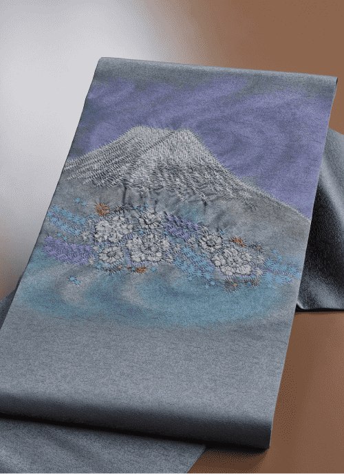 生地には、雪を頂いた山と、ピンクと白の色合いで咲き誇る桜の前景が刺繍されています。背景は紫と青の柔らかなグラデーションで、穏やかな風景を引き立てています。質感が豊かで、作品に深みを与えています。.