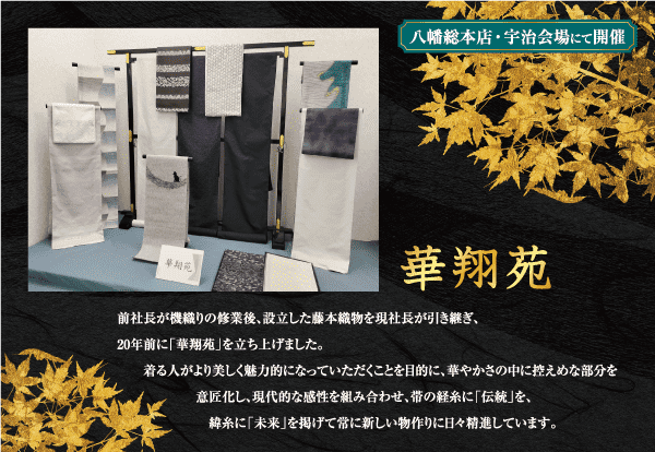 展示では、青とグレーのさまざまな色合いの日本の伝統的な織物が垂直に吊るされています。織物の下には「華翔苑」と題された銘板が中央に掲げられています。黒の背景に金色と白のアクセントが付いた日本語の文字と、イベントの詳細が記されています。