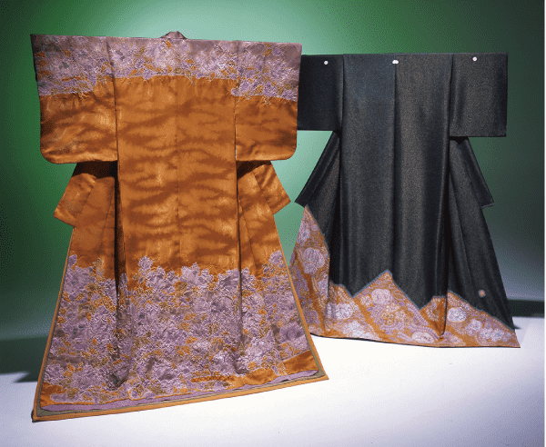 2 着の伝統的な着物が、緑のグラデーションの背景に展示されています。左の着物は濃い琥珀色で、縁にはラベンダー色の複雑な花柄が施されています。右の着物は濃い緑色で、裾には同様のラベンダー色の花柄が施されています。.