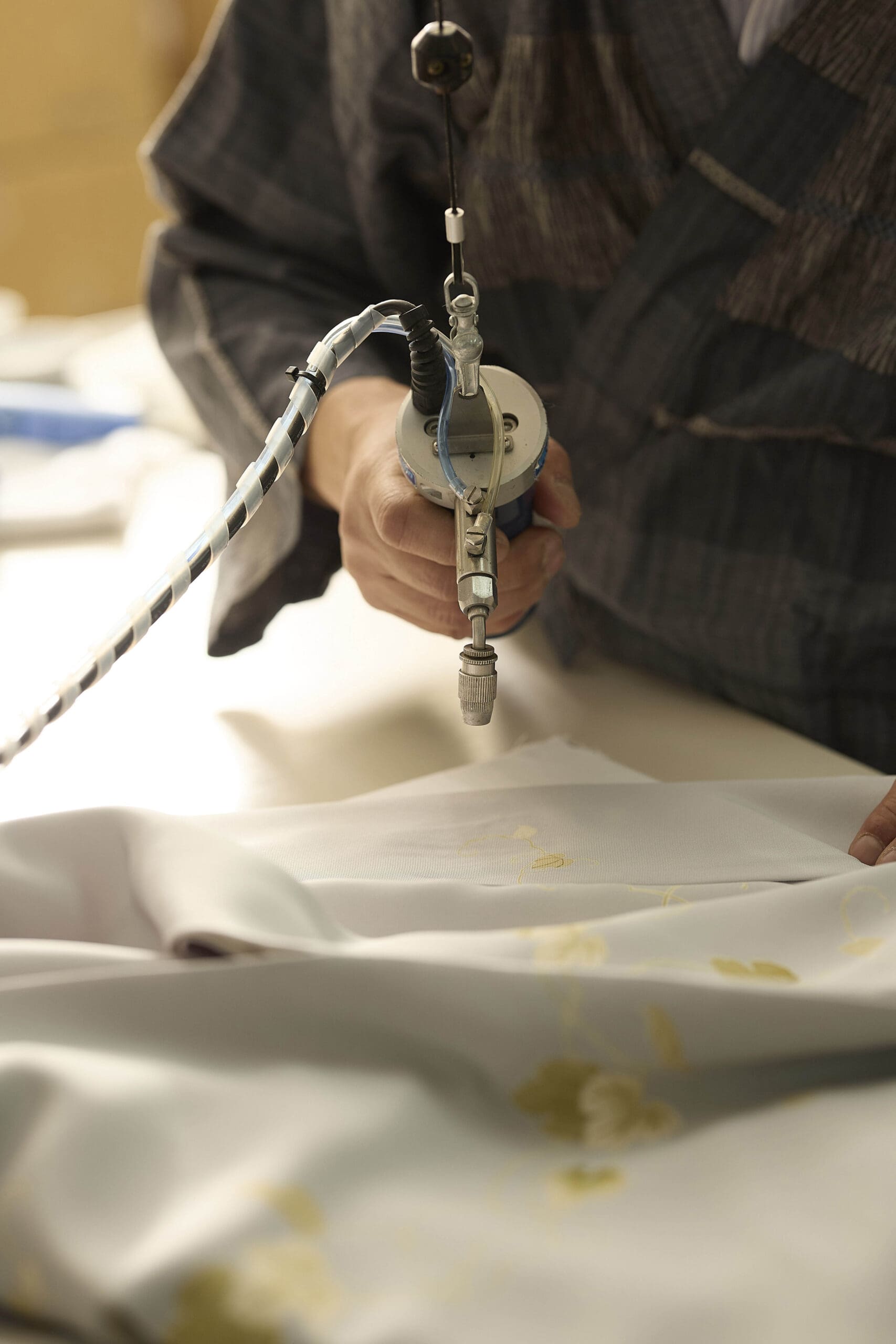 縞模様の服を着た人物が、かすかな黄色いシミのついた白い布地を、手持ちのスプレー道具を使い、集中してクリーニングまたは処理している。このシーンは、注意深く正確な布地の修復やクリーニング作業を示唆している。.